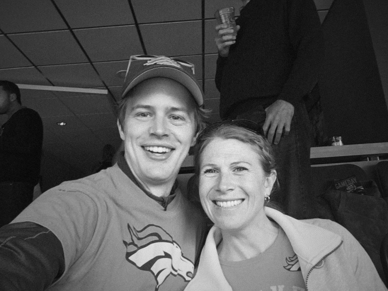 Kaley and Nate smiling together in Denver Broncos orange at a football game.